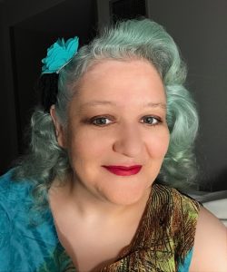 A picture of Molly Burkhart, with lovely blue hair, smiling at the camera.